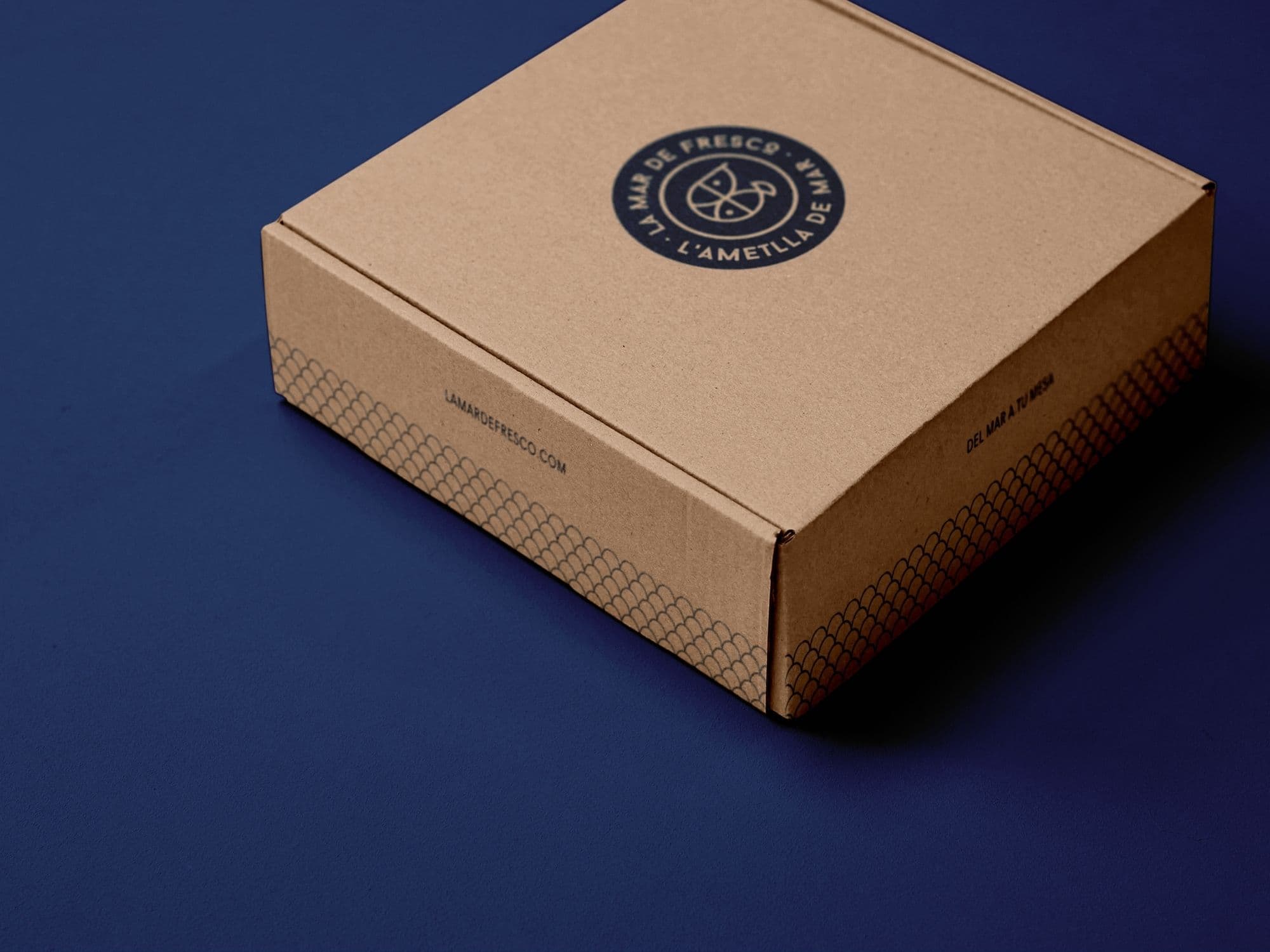 Caja de envío en cartón kraft de La Mar de Fresco con el sello, el patrón de escamas y el lema del mar a tu mesa
